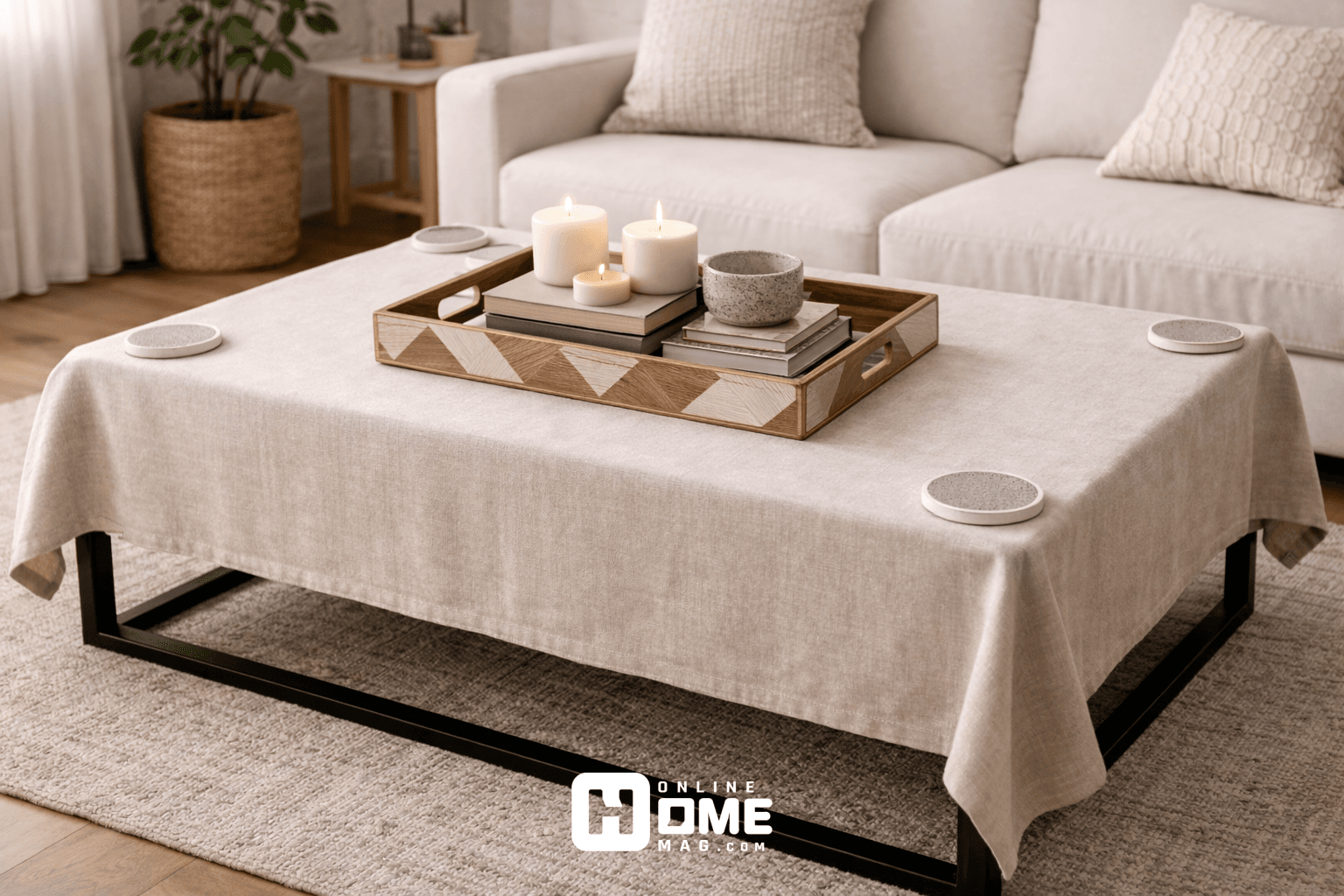 A coffee table with a neutral-colored tablecloth, topped with a stylish geometric tray holding a set of candles and books