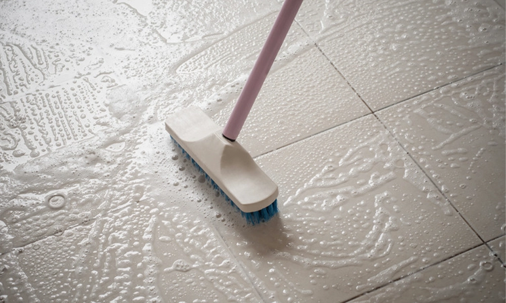 Scrubbing tile floor with a brush and cleaning foam for deep cleaning.