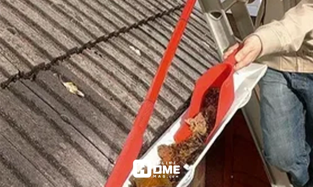 Alt text: "Person cleaning roof gutter using a red gutter cleaning brush to remove leaves and debris."