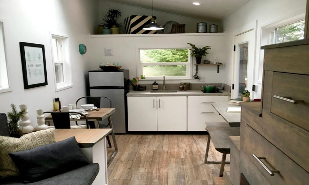 A compact kitchen and dining area with modern white cabinetry, small dining tables, and shelves filled with plants and decor, creating a fresh and functional space.