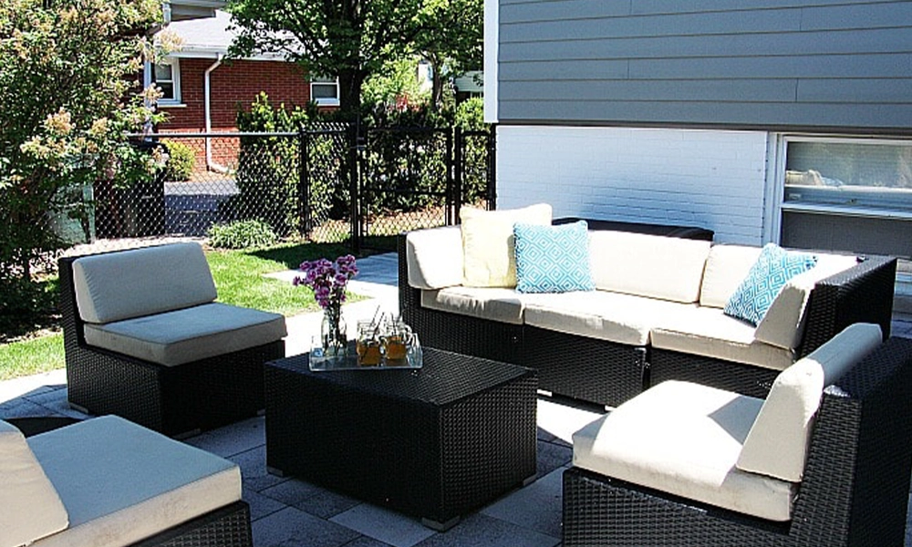 A well-arranged outdoor seating area with black wicker furniture, colorful cushions, and a neat yard.