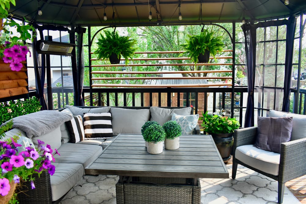 Comfortable outdoor seating with cushions and plants in a gazebo on a small patio, perfect for relaxation.