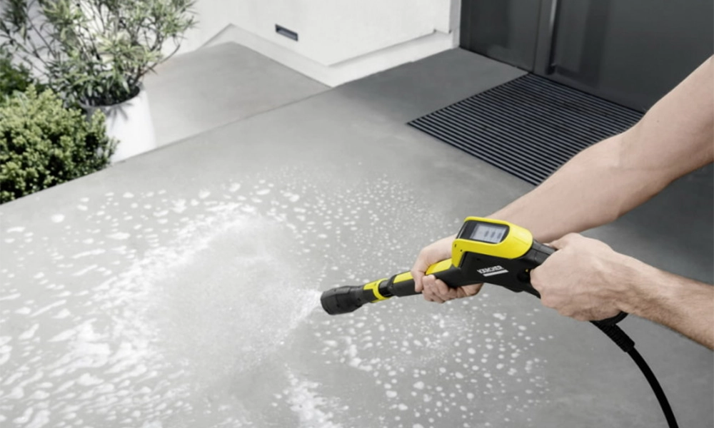 "Person cleaning an outdoor concrete surface using a yellow and black pressure washer releasing steam and water."